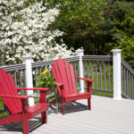 A grey painted deck with red chairs in front of white flowers